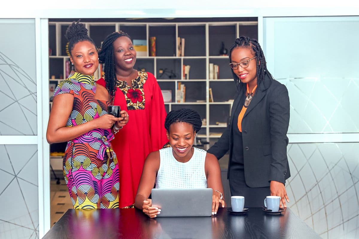 Four professional women collaborating around a laptop in an office