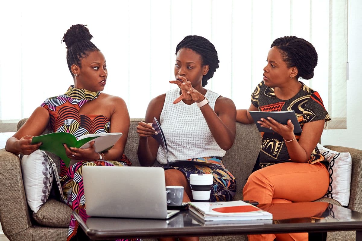 Three women in conversation with notebooks and a laptop